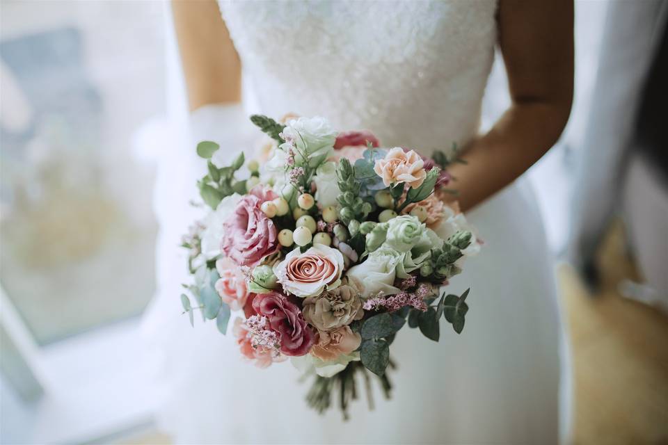 novia sostiene un ramo de flores con rosas y hojas verdes