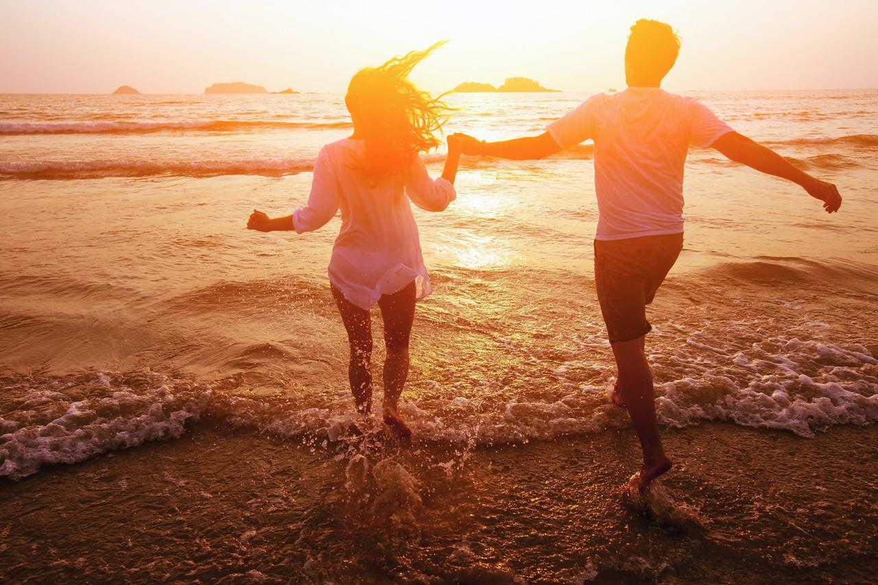 pareja tomada de la mano a la orilla del mar con luz dorada de fondo