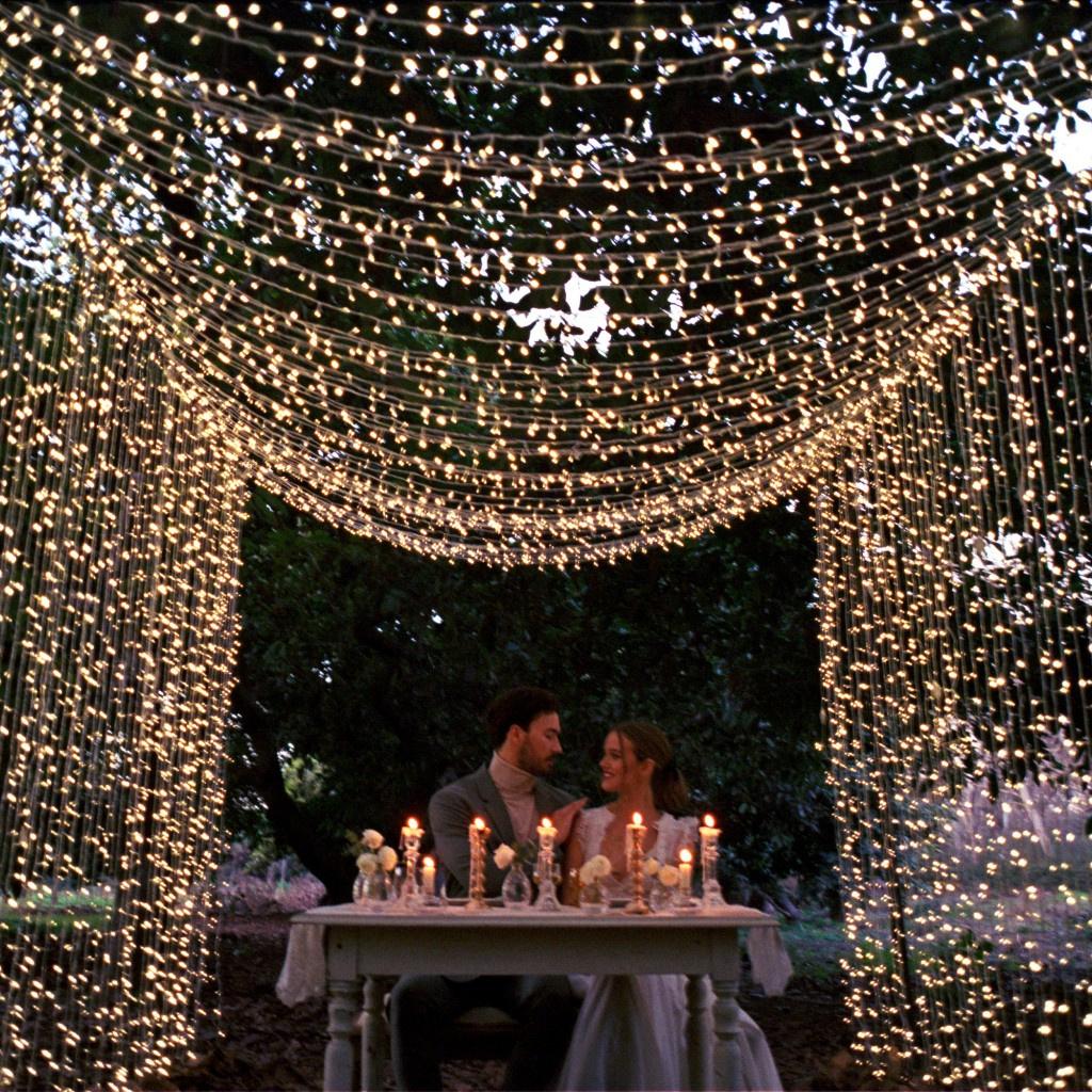 pareja sentada en una mesa con velas y guirnaldas de luces