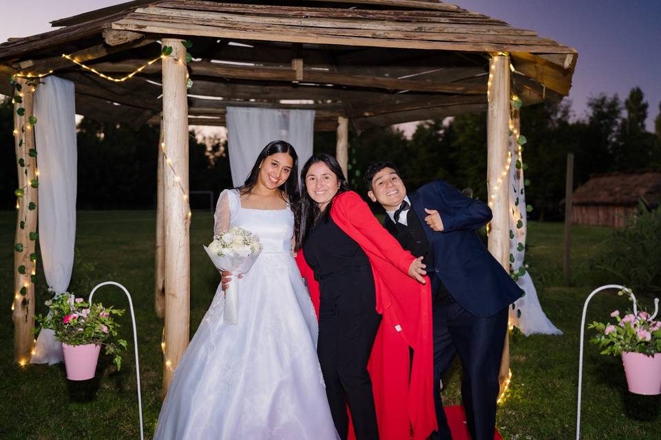 Novios posando con invitada en el jardín de noche