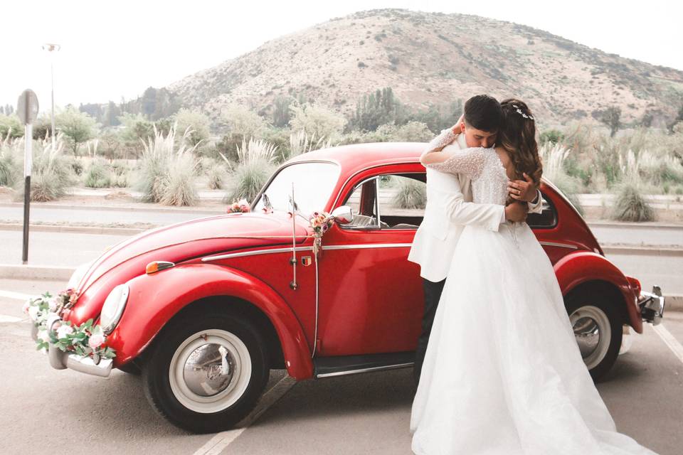 Pareja abrazada frente a un auto rojo