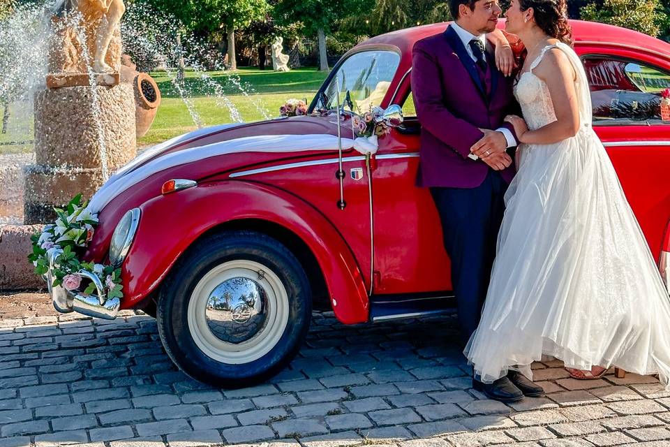 Pareja besándose a lado de un auto rojo