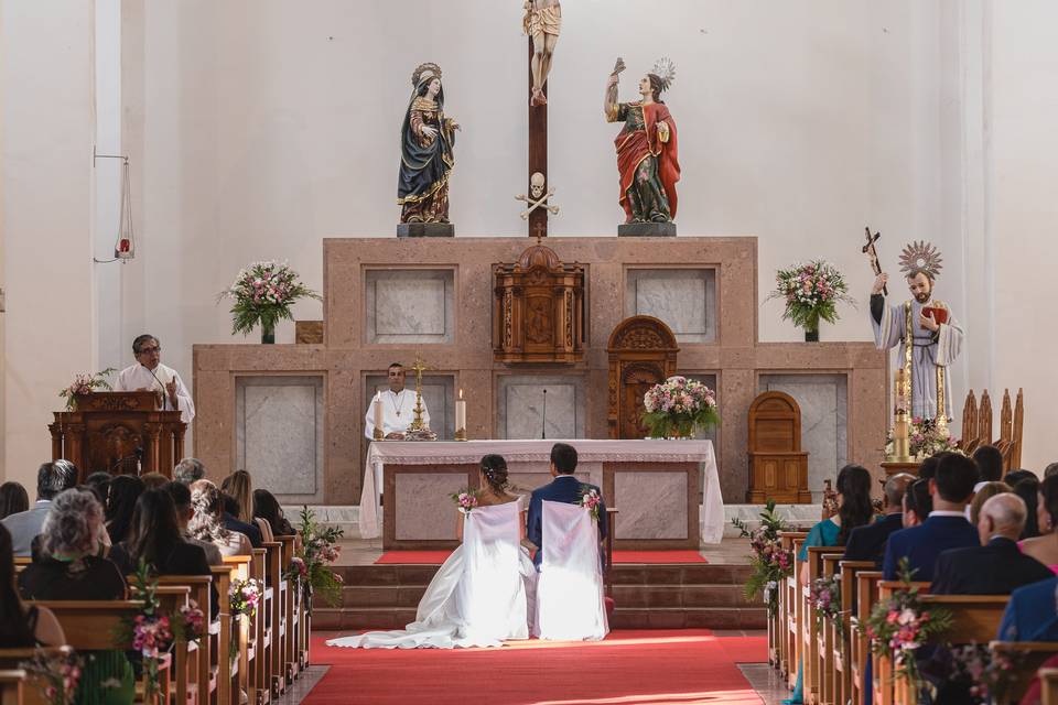 Novios sentados en sillas blancas en la iglesia