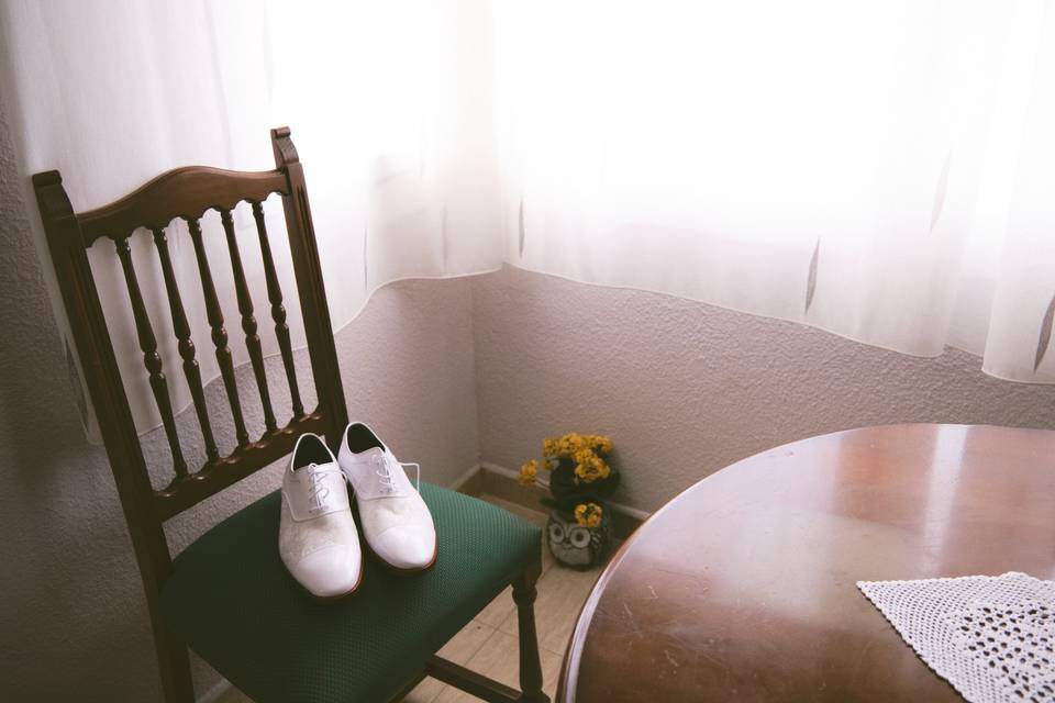 Zapatos blancos sobre una silla a lado de una mesa de madera