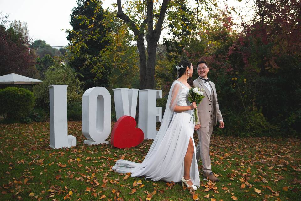 Pareja caminando en el jardín enfrente de las letras blancas