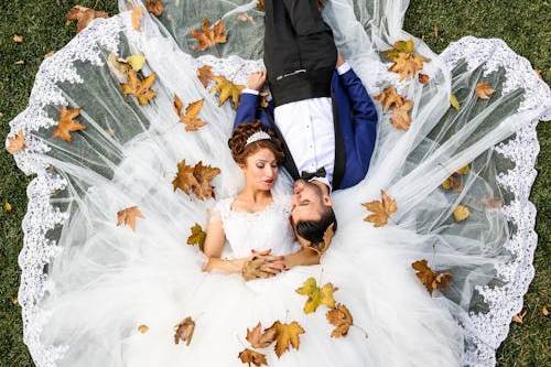 Novios acostados en el pasto con hojas sobre el vestido